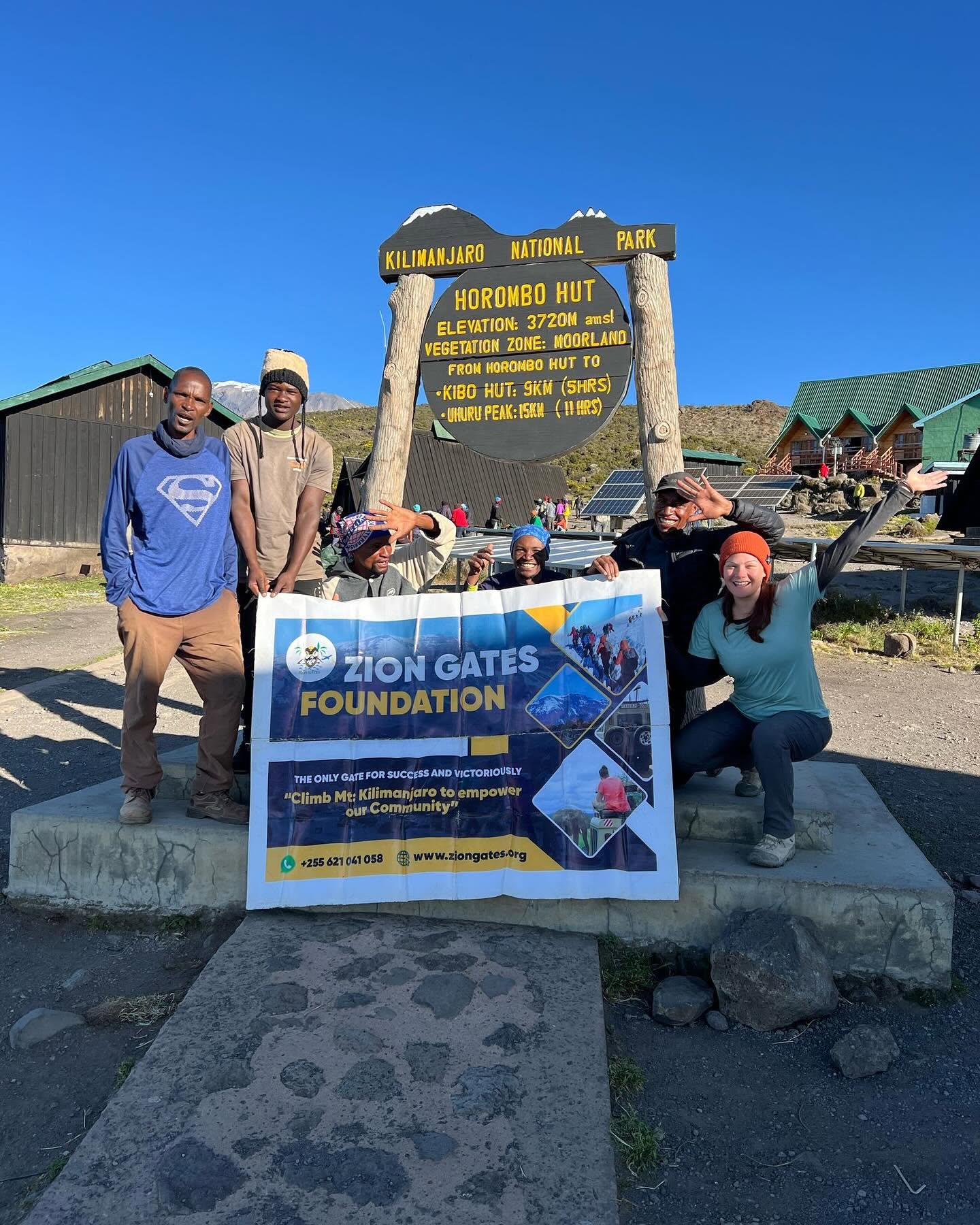 Guides and a guest with a Zion Gates banner at Horombo Hut
